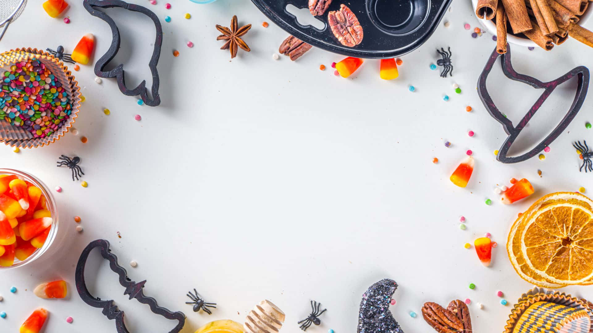 Halloween Cookie Cutters 桌布 壁紙 — 一個節日萬聖節平面擺設，以糖果玉米餅乾模具、乾燥柳橙片和糖針圍繞一個空白白色中心排列。
