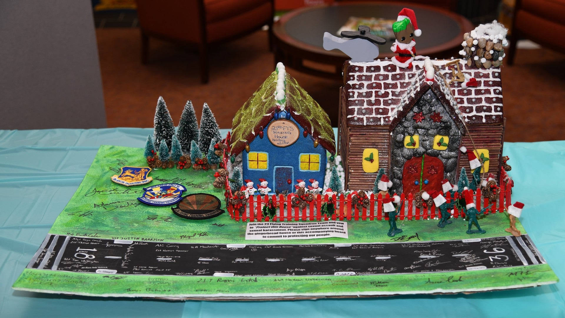 Gingerbread House 桌布 壁紙 — 一個節日薑餅村展示，有兩間精緻的房屋、灑滿雪花的樹木和綠色底座上的小雕像。