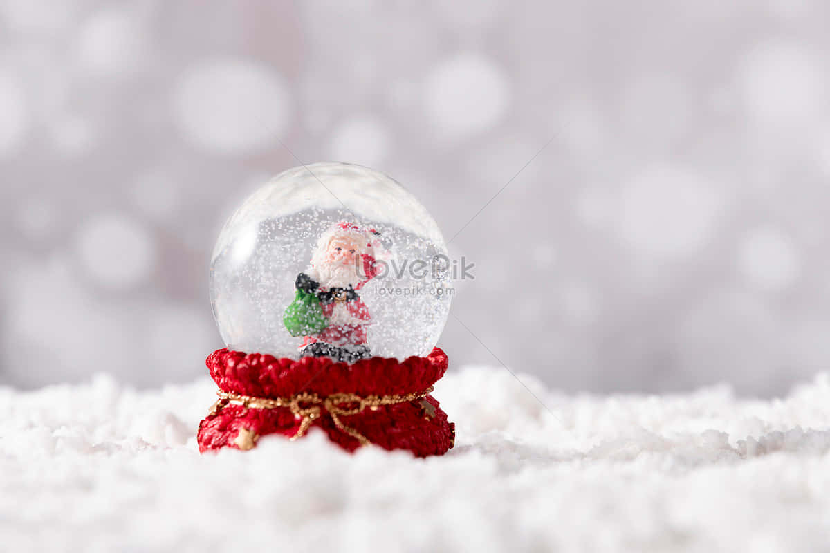 Christmas Snow 桌布 壁紙 — 一個節日雪球，內有一個小聖誕老人公仔，坐在紅色鉤針編織底座上，周圍是蓬鬆的白雪。