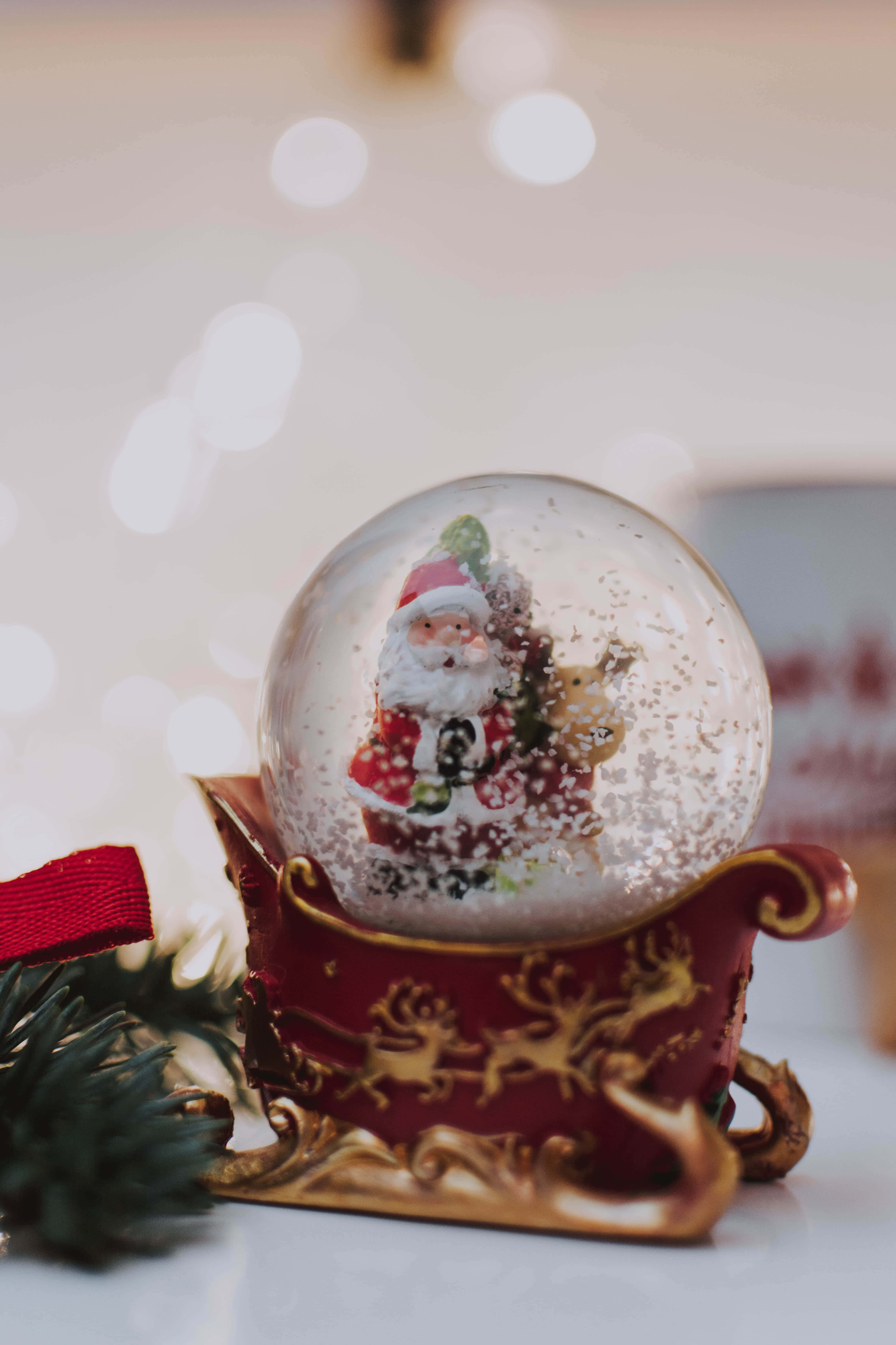 Snow Globe 桌布 壁紙 — 一個節日雪球，裡面有聖誕老人坐在雪橇上，雪花飄落，旁邊放著松樹枝和紅色絲帶。