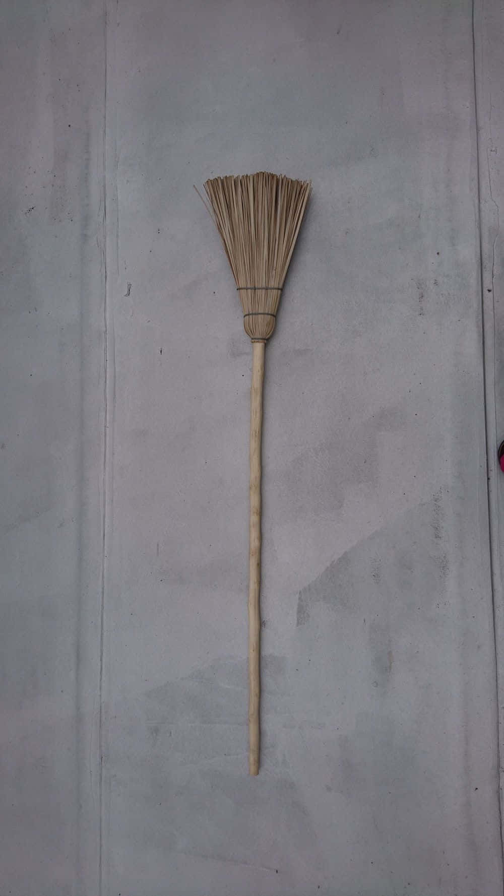 工具 桌布 壁紙 — 一個簡單的稻草掃帚，帶有木柄，垂直掛在素色灰色混凝土牆上。
