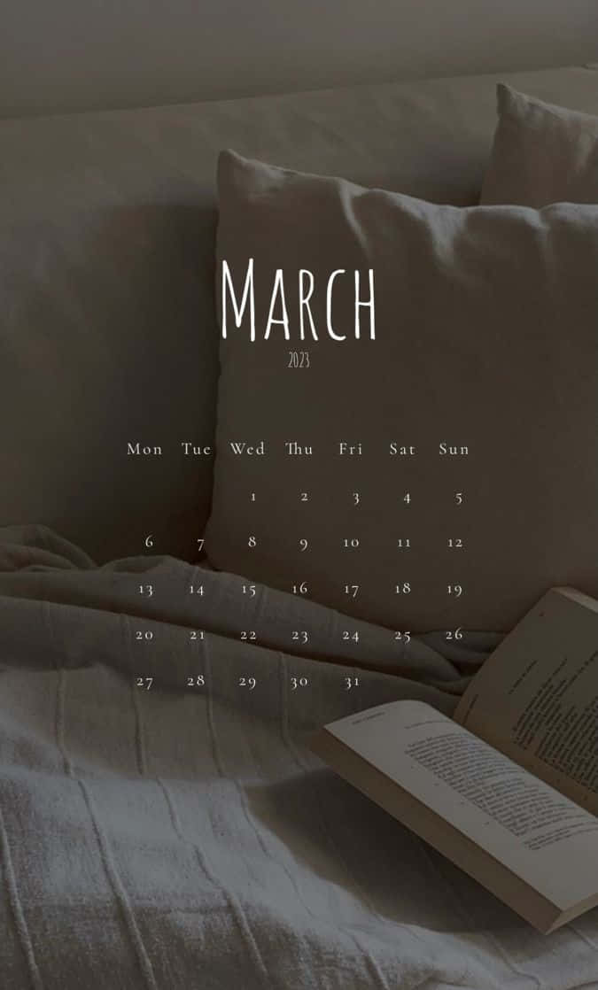 March 桌布 壁紙 — 一個簡約的2023年3月月曆放在舒適床上的柔軟米色枕頭上，旁邊有一本打開的書。