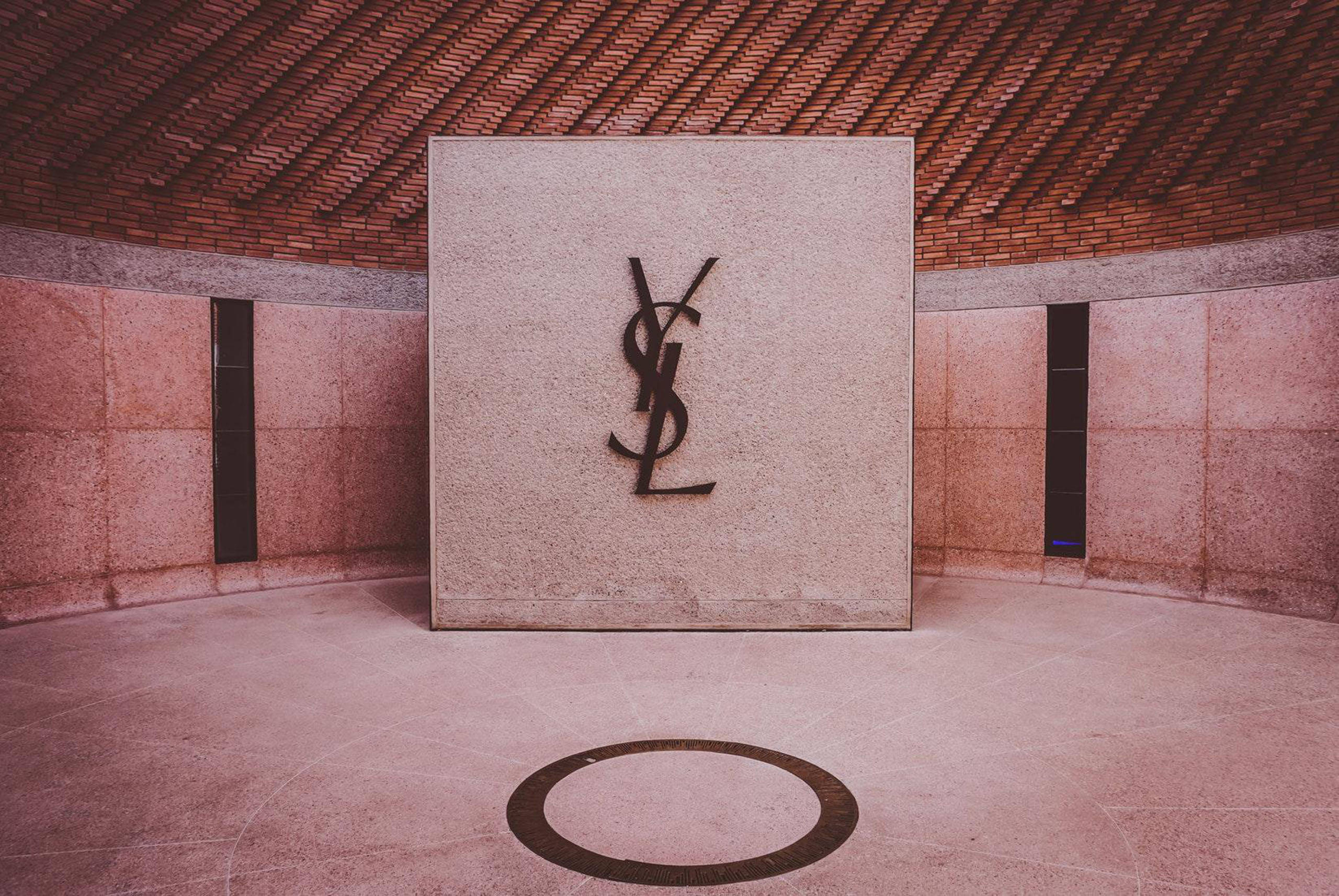 YSL 桌布 壁紙 — 一個簡約的室內空間，在紋理磚天花板下的石牆上有一個大型YSL標誌。