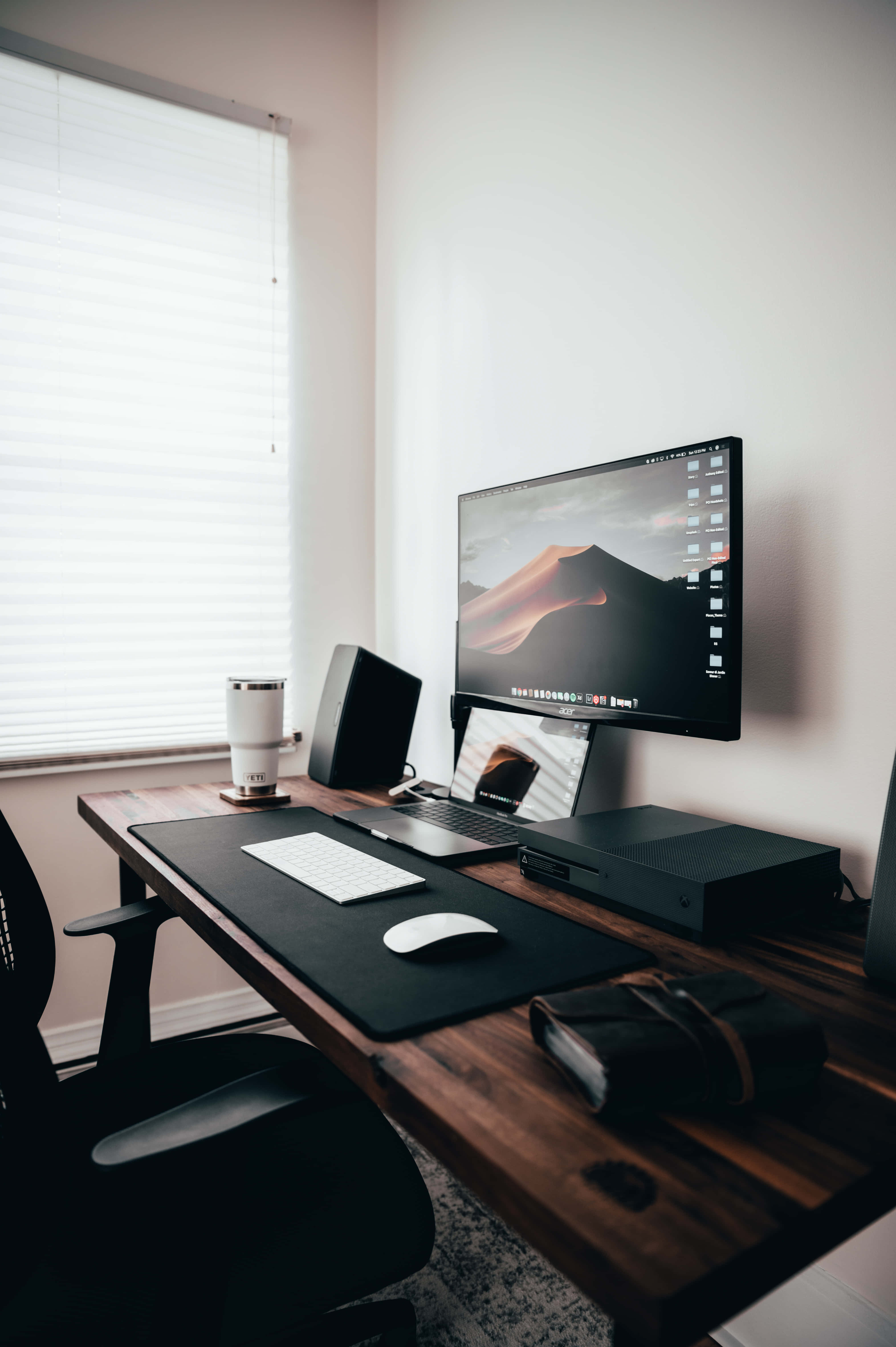 Desk 桌布 壁紙 — 一個簡約的家庭辦公室，配有木桌、黑色椅子和時尚的科技設備，從帶百葉窗的窗戶灑進柔和自然光。