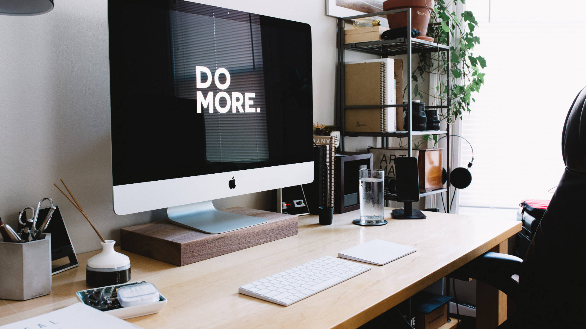 Working From Home 桌布 壁紙 — 一個簡約的家用辦公桌，配備時尚的iMac顯示'DO MORE.'，周圍環繞植物和現代科技。