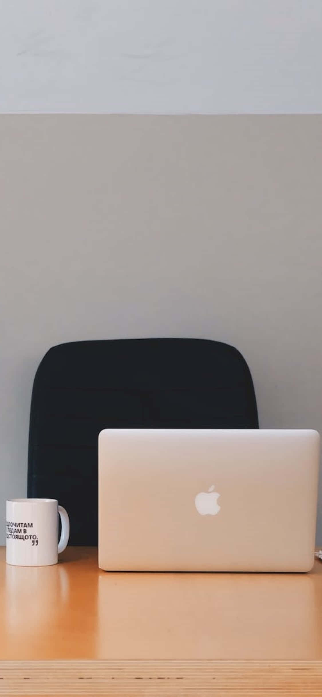 Desk 桌布 壁紙 — 一個簡約的工作空間，木桌上放著金色筆記型電腦和白色馬克杯，背景是素色牆壁。