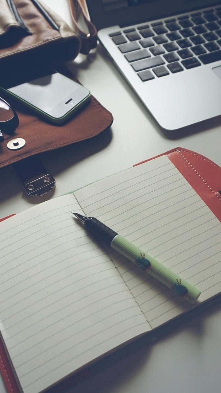 Diary 桌布 壁紙 — 一個簡約的工作空間，筆記本、筆、筆記型電腦和電話整齊地擺放在潔白的桌子上。