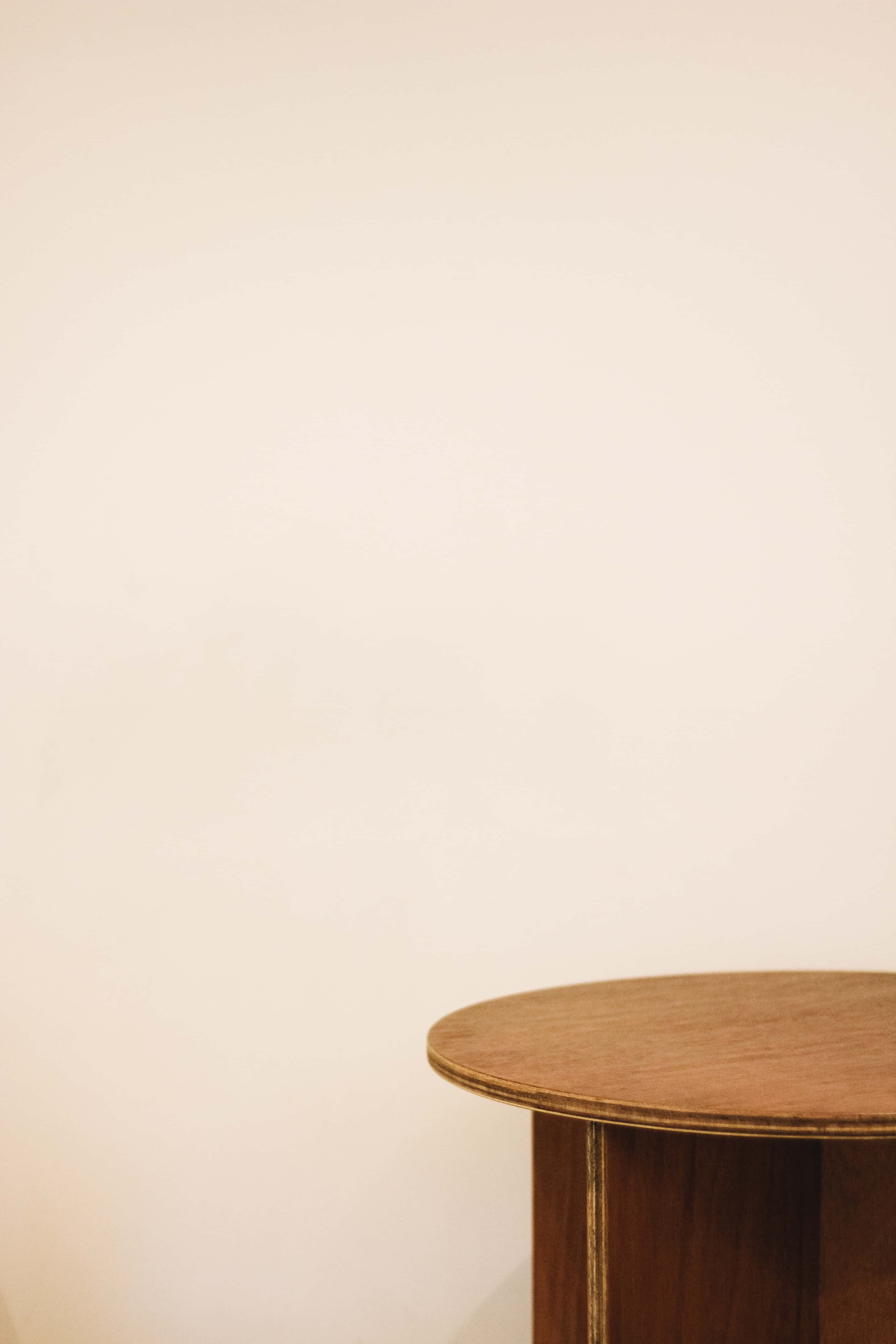 table 桌布 壁紙 — 一個簡約的木桌角靠在柔軟的米色牆上，位於寧靜的室內空間。