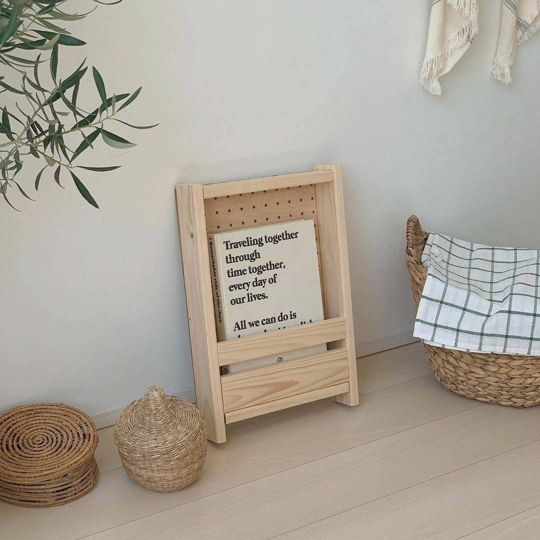 Beige Minimalist 桌布 壁紙 — 一個簡約的木牌上寫著一句窩心的語錄，靠牆放在編織籃子和橄欖枝旁邊，營造出寧靜的室內角落。