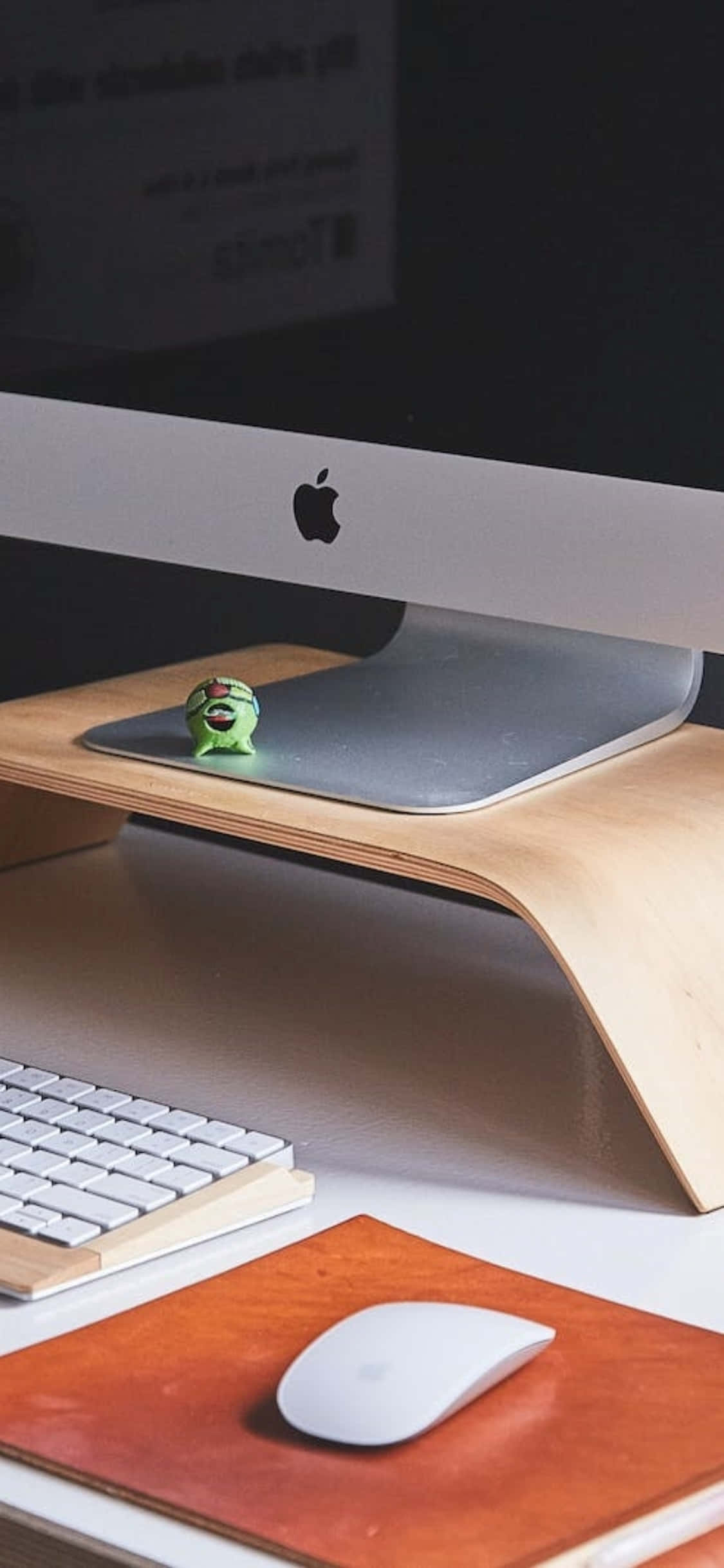 Desk 桌布 壁紙 — 一個簡約的桌面設置，包括 Apple iMac、白色鍵盤和滑鼠放在木製支架上，並有一個綠色小公仔。