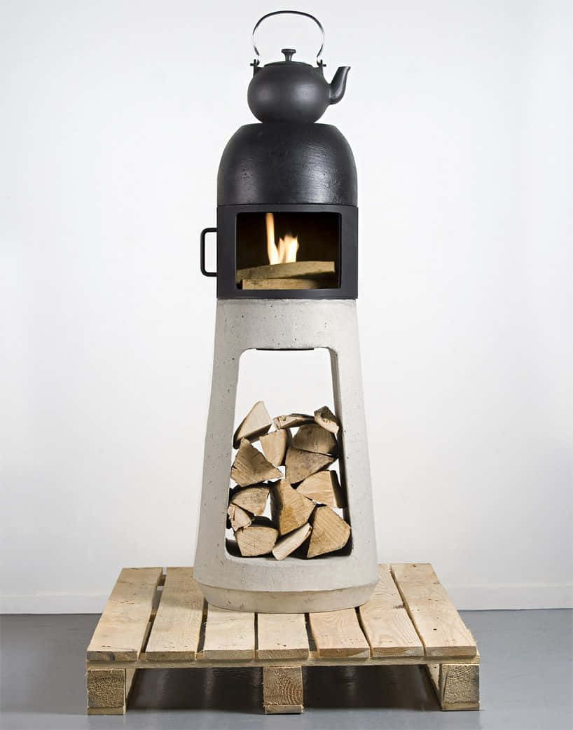 Stove 桌布 壁紙 — 一個簡約的混凝土壁爐，上面有燃燒的木柴和一個黑色茶壺，放在木托盤上，靠著白色牆壁。