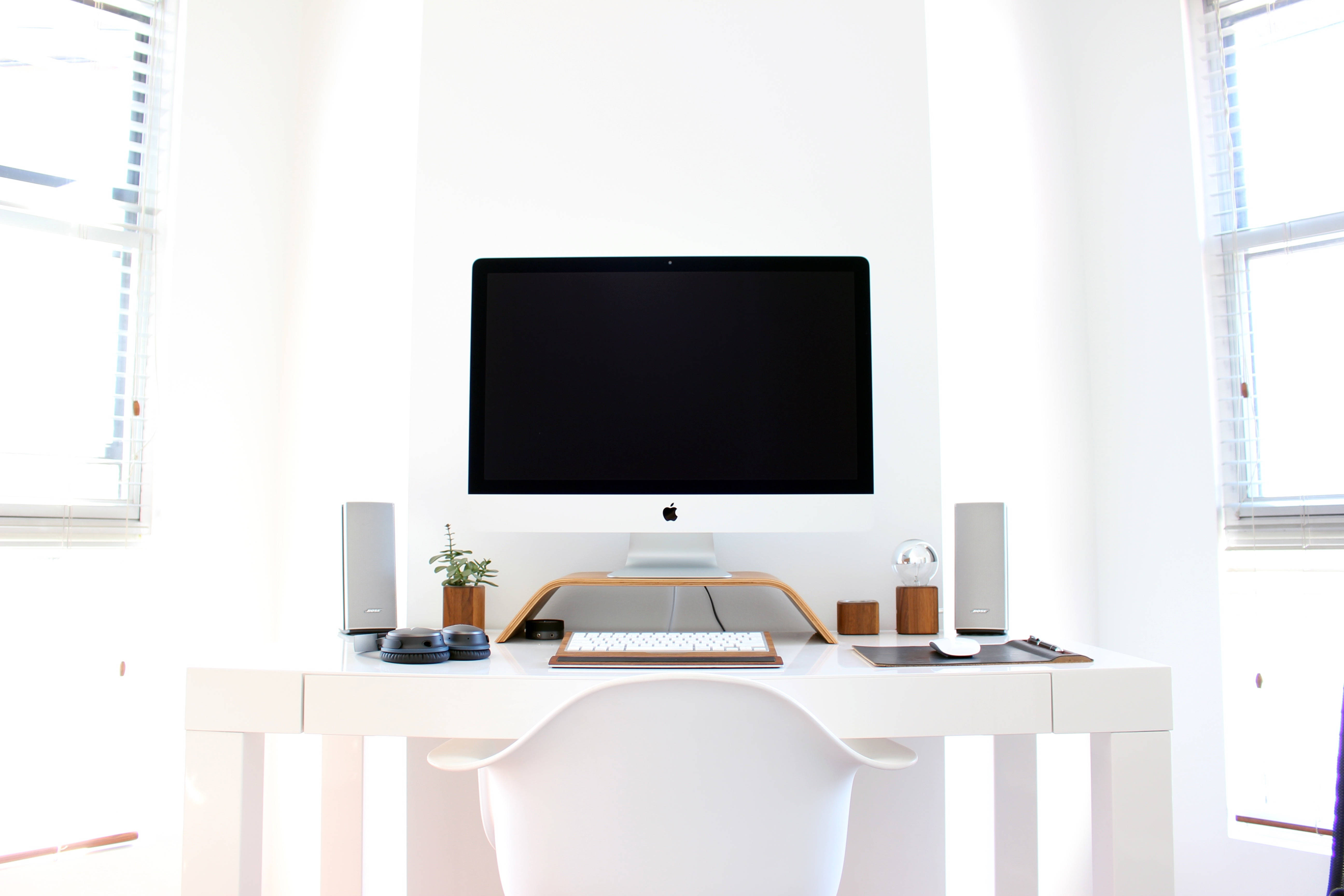 Mac 桌布 壁紙 — 一個簡約的白色家庭辦公室，配備時尚的 iMac 設置，沐浴在大窗戶透入的明亮自然光中。