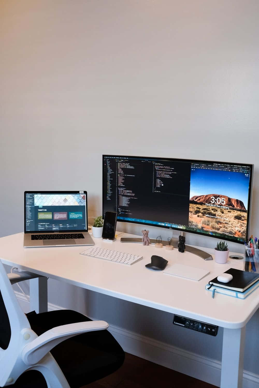 Desk 桌布 壁紙 — 一個簡約的白色桌面設置，雙顯示器一個顯示程式碼另一個顯示沙漠桌布，旁邊有一台筆記型電腦和黑色人體工學椅。