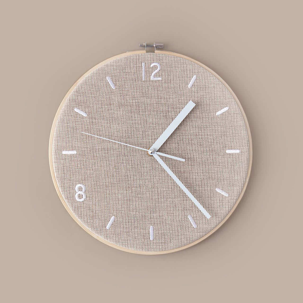 Clock 桌布 壁紙 — 一個簡約的米色亞麻壁鐘，帶有白色指針和數字，居中掛在相配的牆上。