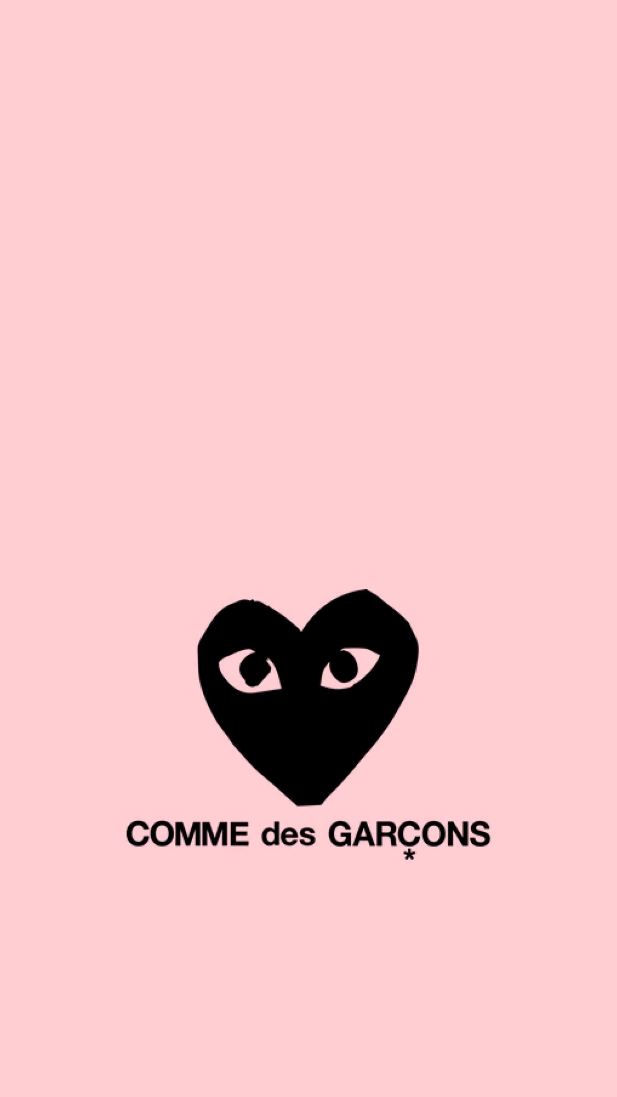 cdg 桌布 壁紙 — 一個簡約的粉紅色背景，上面有一個帶眼睛的黑色心形標誌，下方是品牌名稱 COMME des GARÇONS。