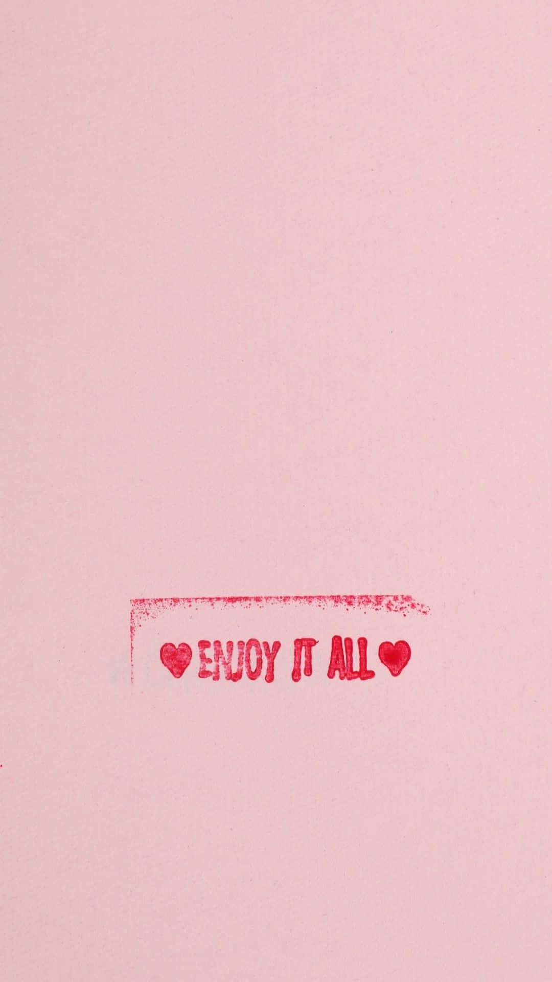 語錄 桌布 壁紙 — 一個簡約的粉紅色背景，上面有紅色蓋印文字 enjoy it all，兩側有心形圖案。