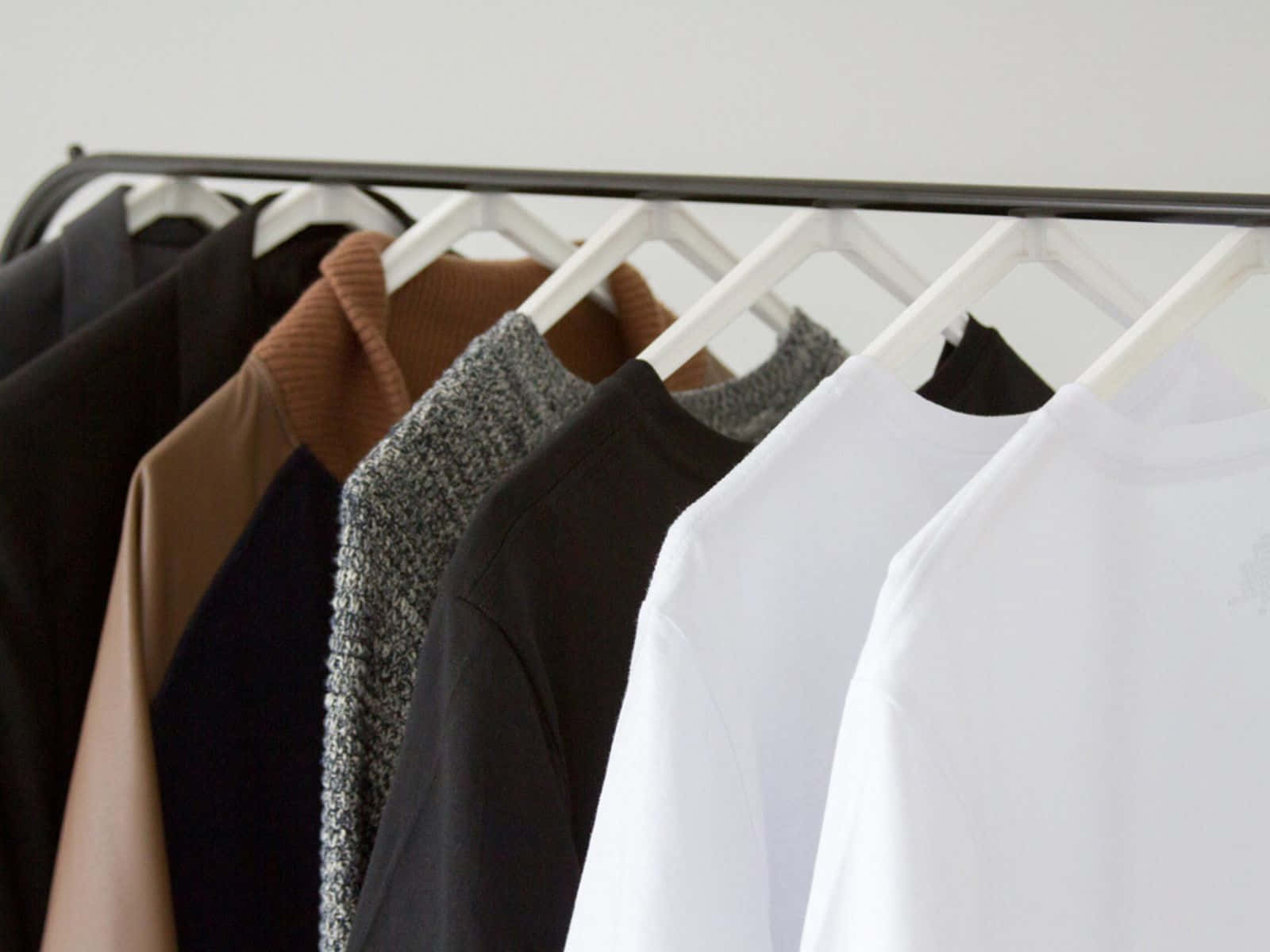 Clothes 桌布 壁紙 — 一個簡約的衣架展示了一排精心挑選的中性色調衣物，從深色到淺色，在柔和自然光下。
