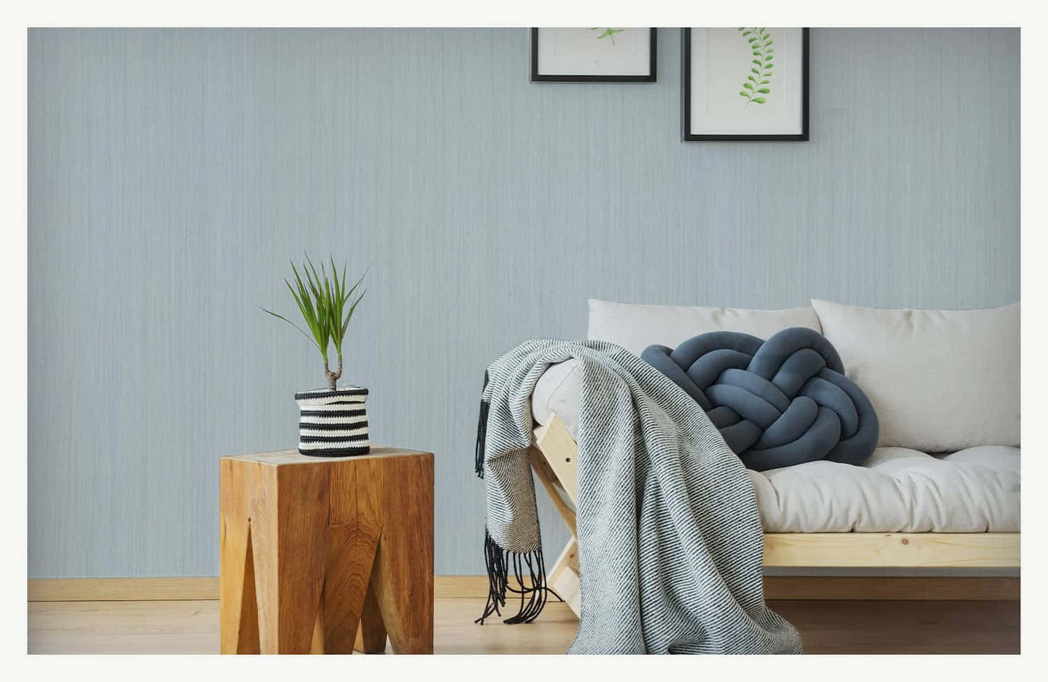 Wall Painting 桌布 壁紙 — 一個簡約風格的客廳，木質沙發上放著灰色針織毯子和編織枕頭，背景是帶紋理的淺藍色牆壁。