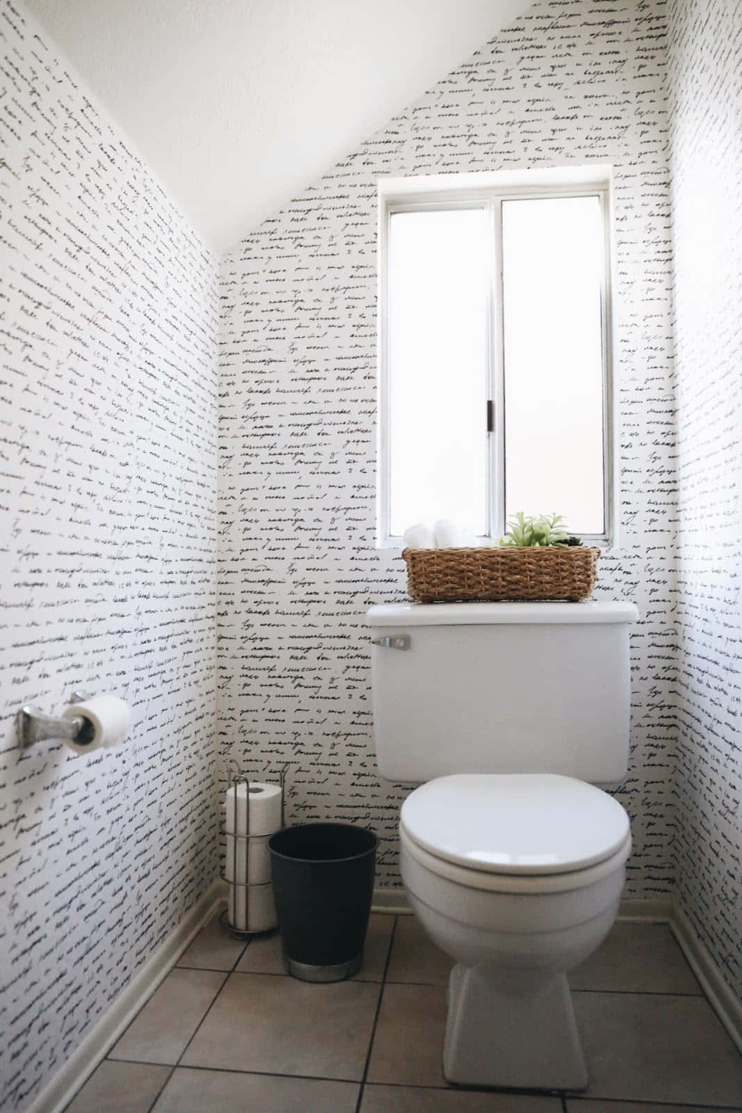 Bathroom Decor 桌布 壁紙 — 一個簡約風格的浴室，配有白色馬桶和瓷磚地板，牆壁覆蓋著優雅的草書字體壁紙，水箱上方窗戶的自然光線。