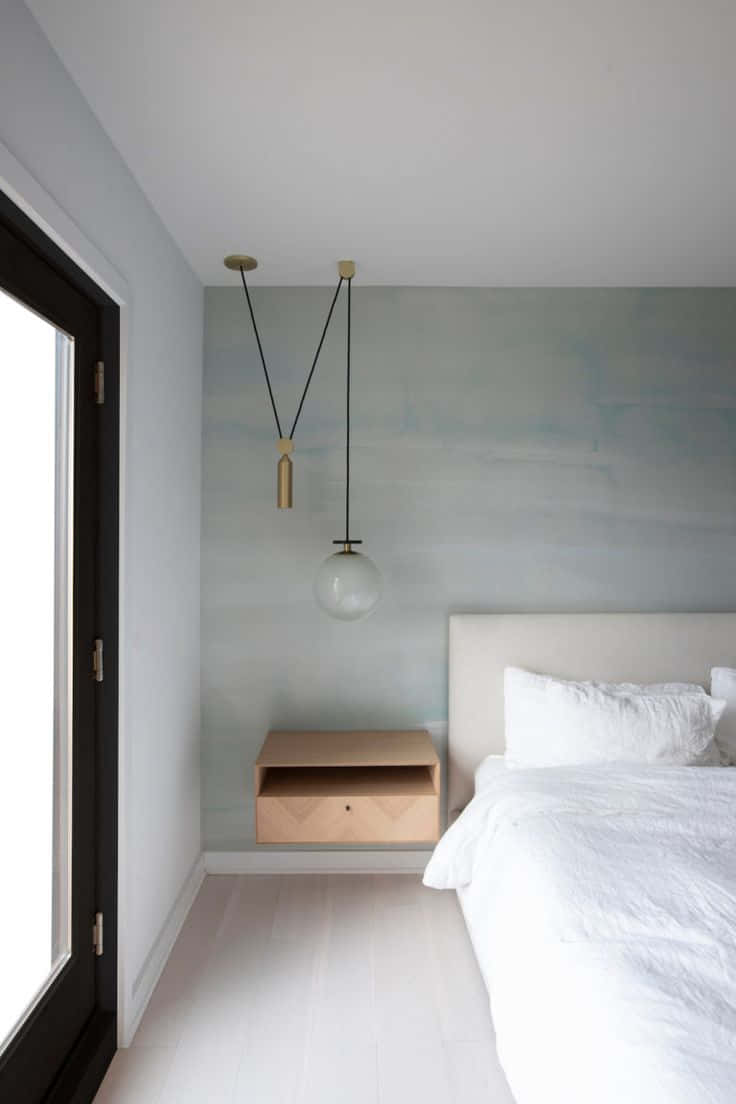 Minimalist Design 桌布 壁紙 — 一個簡約風格的臥室，配有白色床、浮動木床頭櫃和現代吊燈，背景是柔和的灰色牆壁。