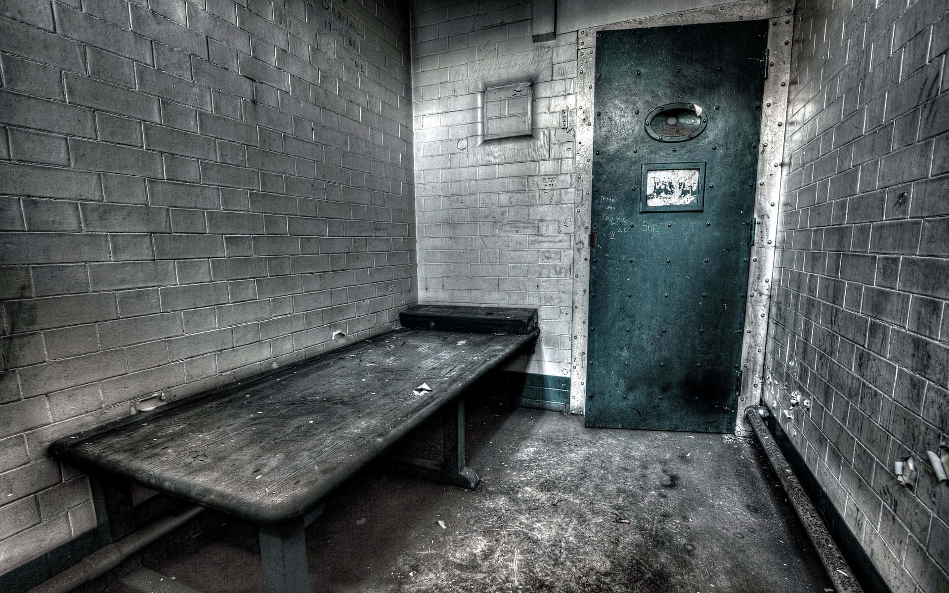 Prison 桌布 壁紙 — 一個簡陋的監獄牢房，內有金屬雙層床和一道顯示老舊與疏忽痕跡的沉重鋼門。