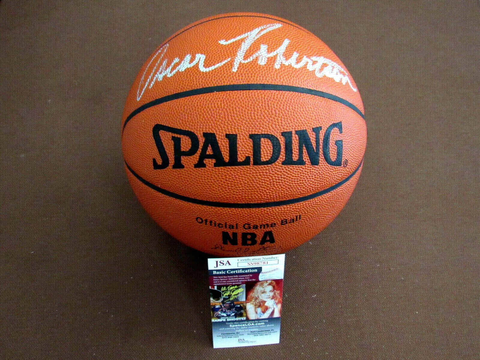 NBA 桌布 壁紙 — 一個簽名的橙色Spalding NBA籃球，上面有白色簽名和JSA認證卡，放在棕色表面上。