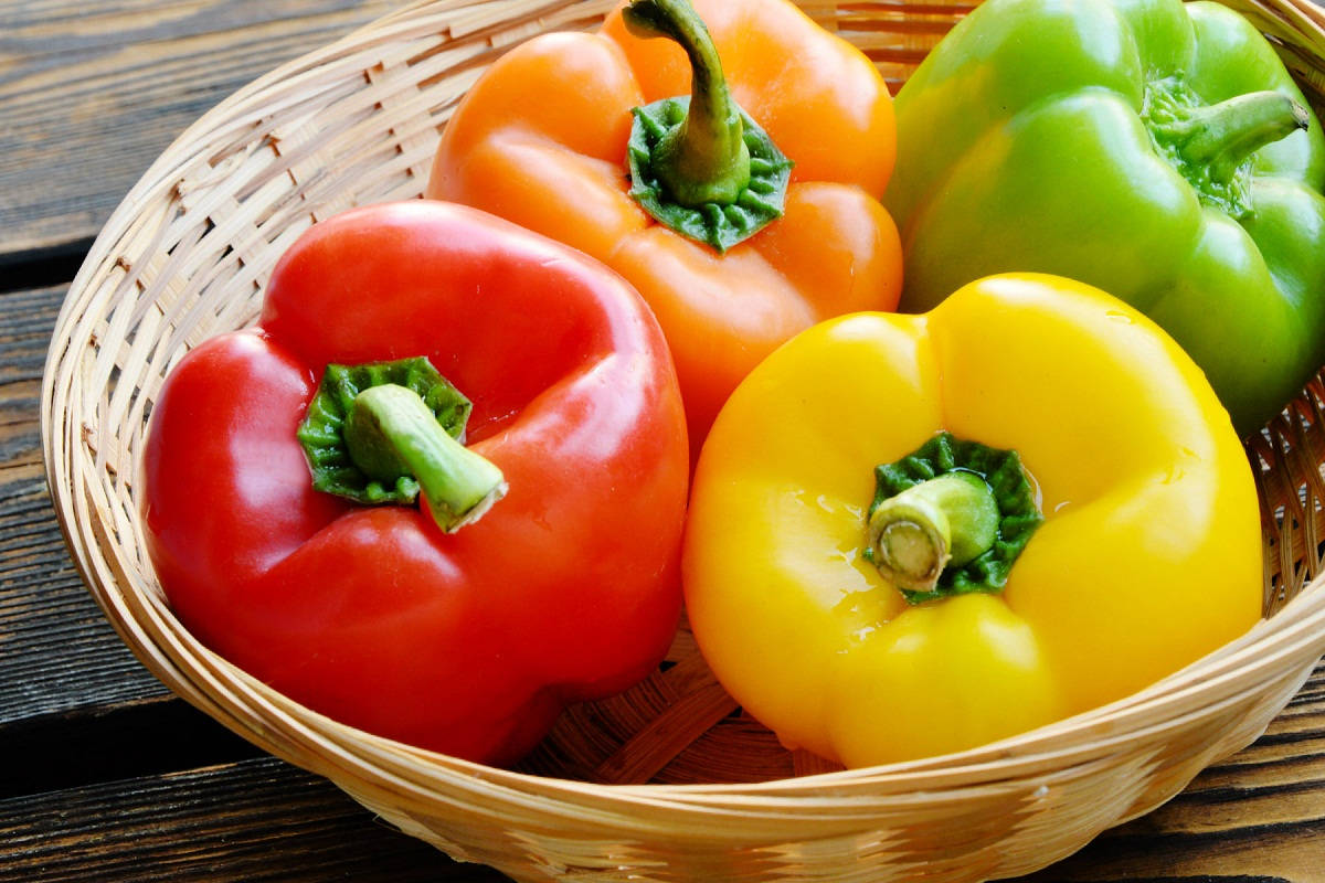 Fruit 桌布 壁紙 — 一個籃子裝著鮮紅、橙、黃和綠色的甜椒，放在質樸的木質表面上。