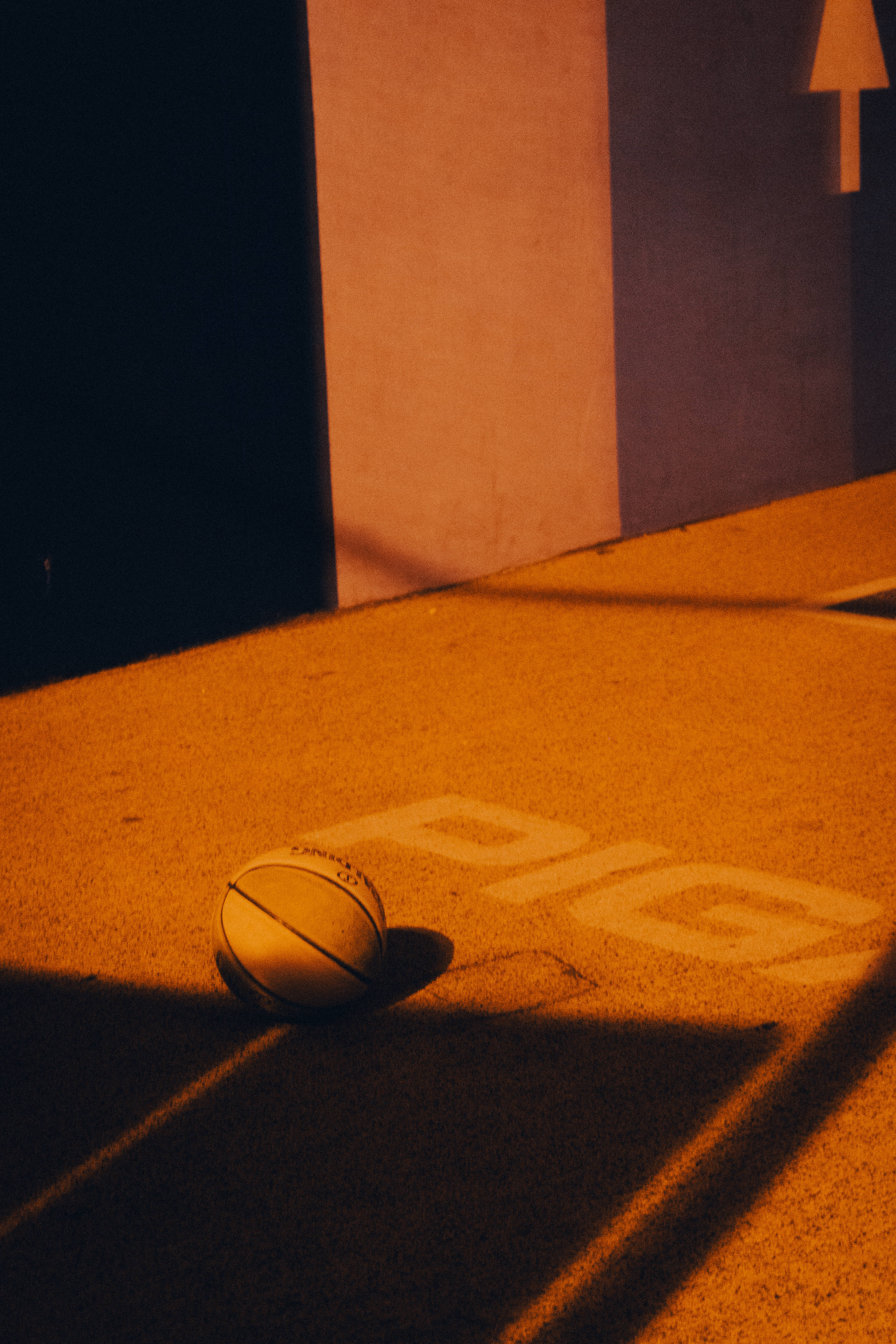 Playground 桌布 壁紙 — 一個籃球在溫暖的橙色光線中，停留在一個帶有粗體字母的球場上，下方有戲劇性的陰影。