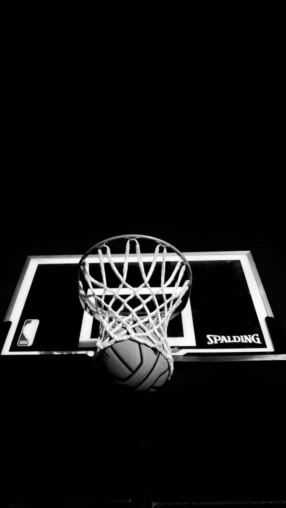 籃球 桌布 壁紙 — 一個籃球掛在 Spalding 籃框上，背景為純黑，呈現高對比黑白效果。