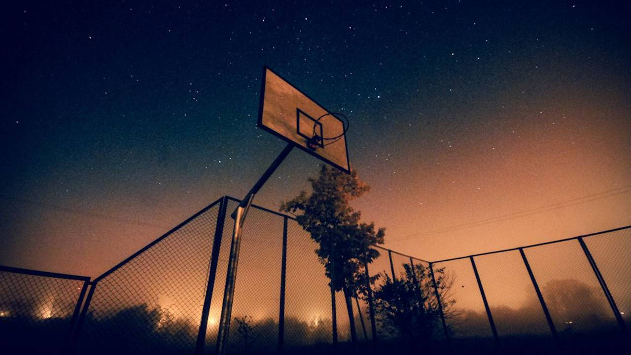  壁紙 — 一個籃球框在星空夜空和地平線上的橙色光芒中呈現剪影。