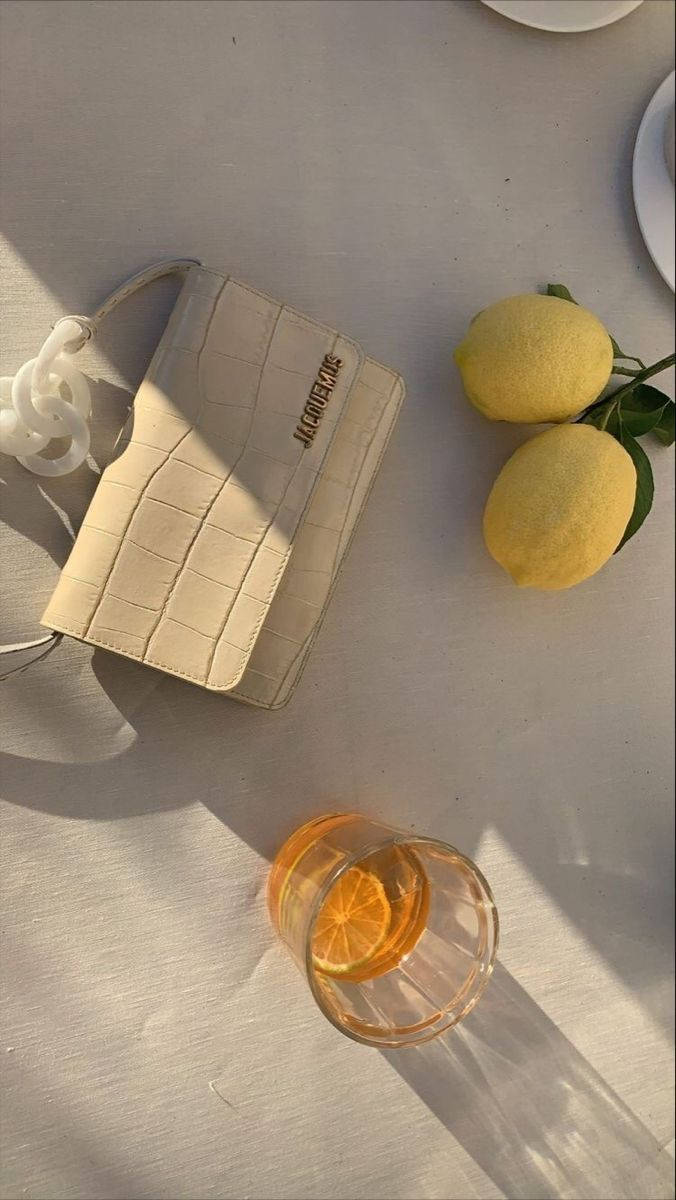 Handbag 桌布 壁紙 — 一個米色鱷魚壓紋手提包和一杯柑橘飲料放在陽光照射的桌巾上，旁邊是新鮮檸檬。