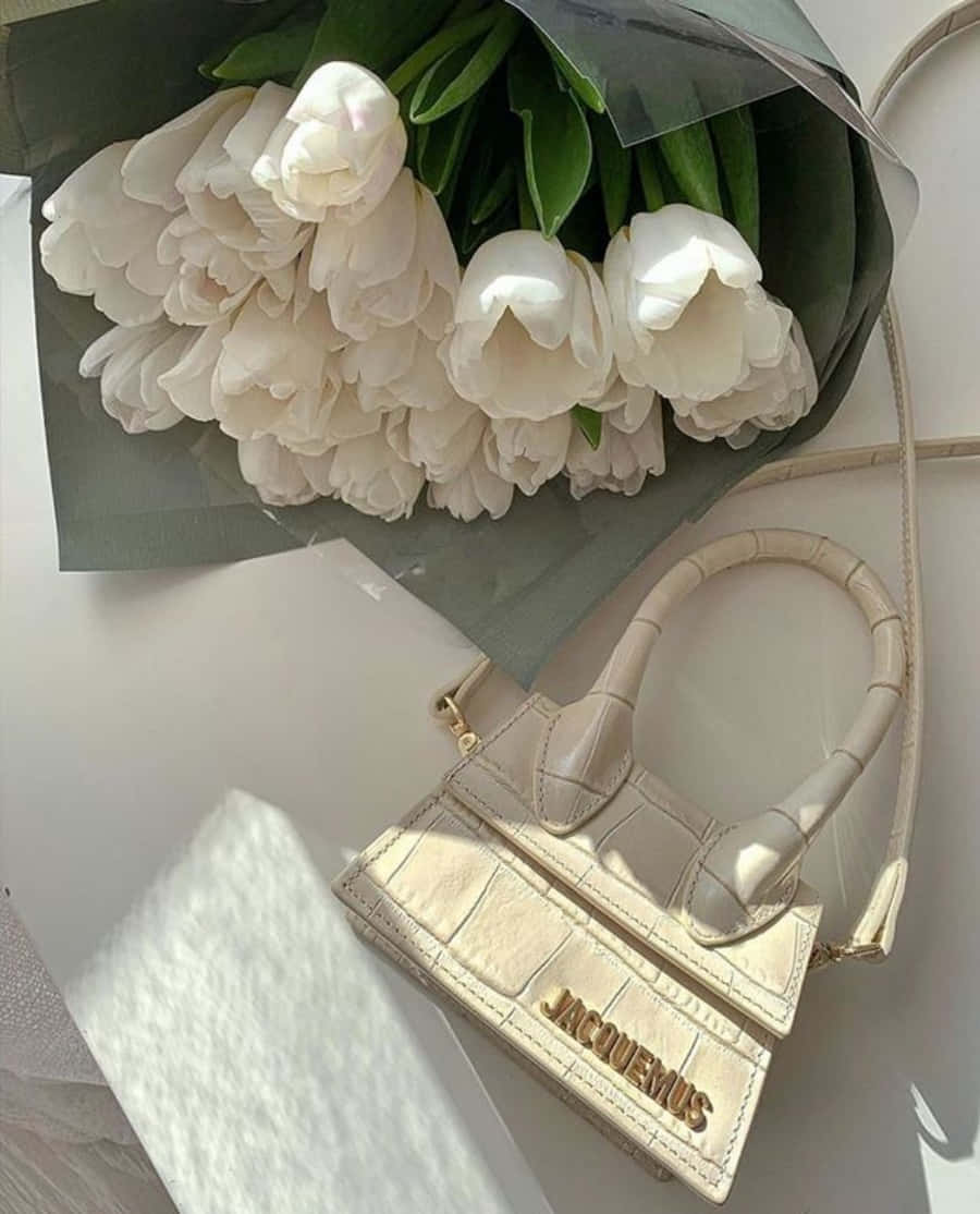 purse 桌布 壁紙 — 一個米色鱷魚紋Jacquemus手提包放在一個明亮的白色表面上，旁邊是一束用深綠色紙包裹的白色鬱金香。