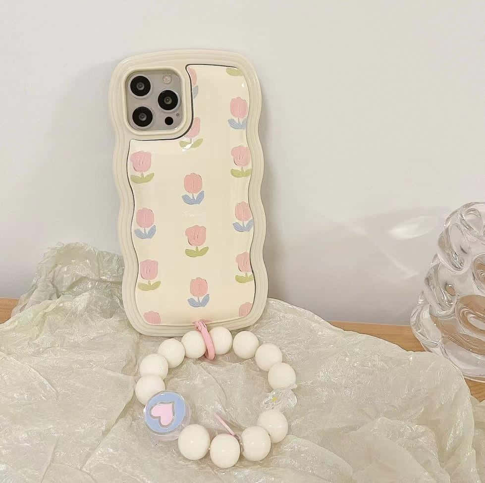 iPhone 美學 桌布 壁紙 — 一個粉彩鬱金香圖案的手機殼放在皺巴巴的塑膠上，旁邊有一個白色珠子手鍊和玻璃花瓶。