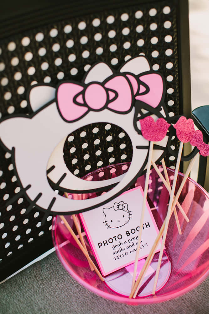 Hello Kitty Party 桌布 壁紙 — 一個粉紅色Hello Kitty攝影棚道具，帶有閃亮的心形棒，放在一個半透明的粉紅色碗中，背景是黑色圓點圖案。