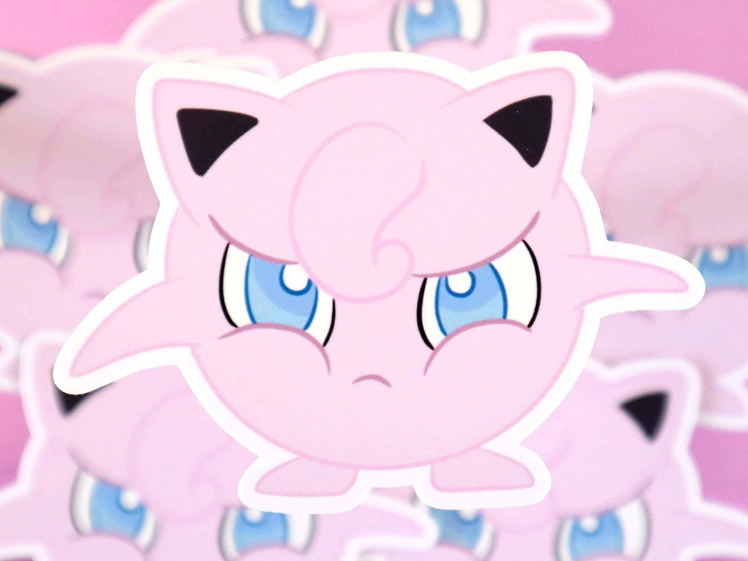Jigglypuff 桌布 壁紙 — 一個粉紅色Jigglypuff貼紙的特寫，有藍色眼睛和皺眉表情，背景模糊，有類似貼紙。