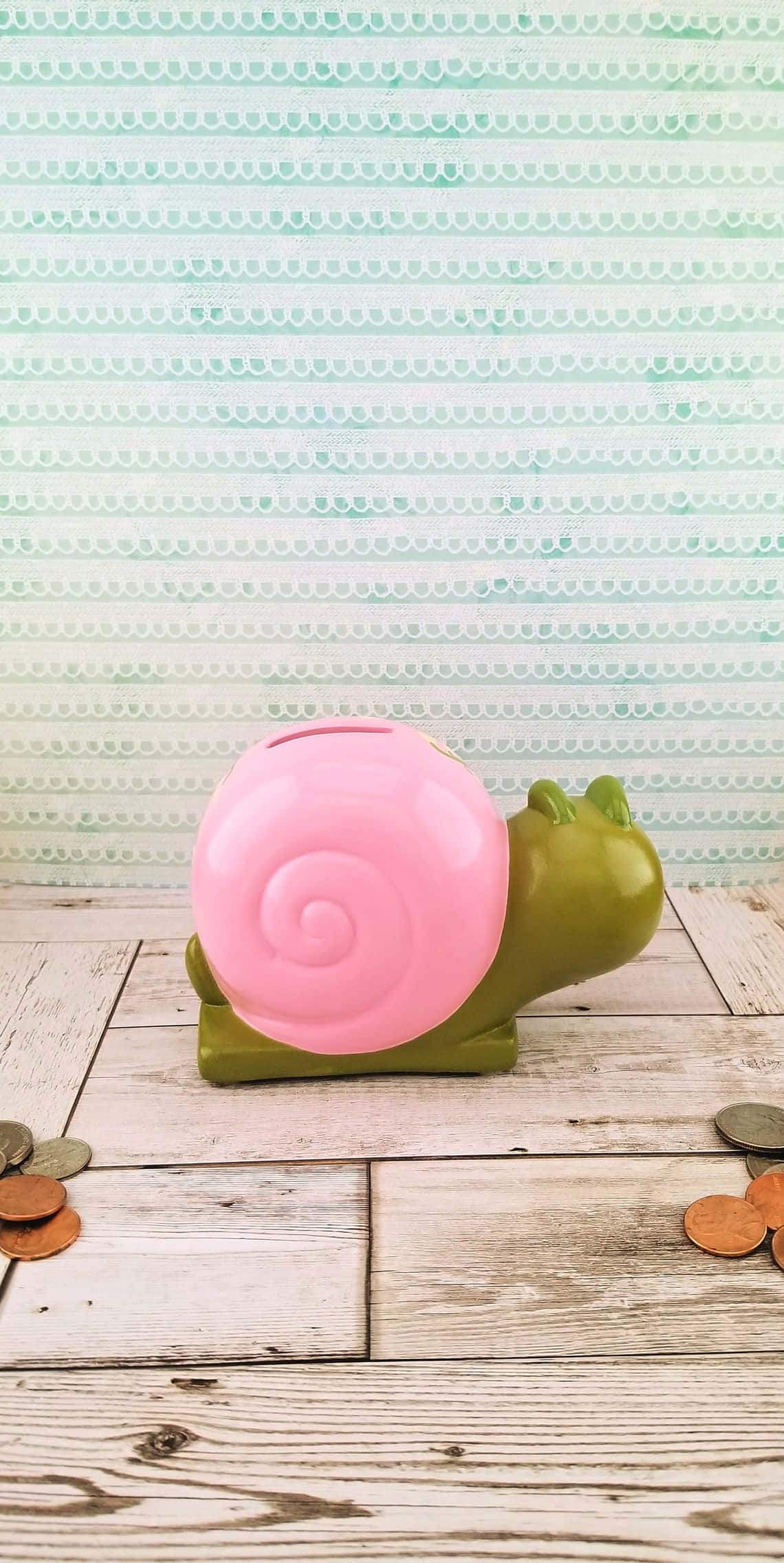 Pink Snail 桌布 壁紙 — 一個粉紅色和綠色的蝸牛形狀小豬撲滿放在一個風化的木質表面上，周圍散落著硬幣，背景是薄荷綠圖案。