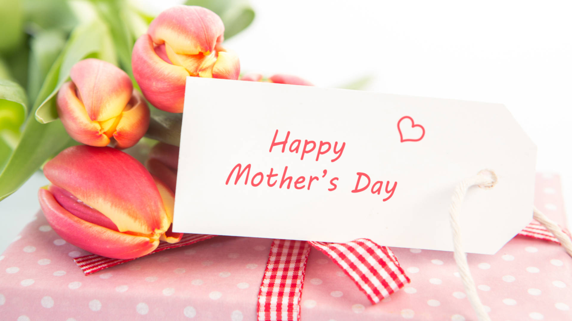 Happy Mothers Day 桌布 壁紙 — 一個粉紅色圓點禮物，用紅色格子絲帶包裝，旁邊有鬱金香和一個「Happy Mother's Day」標籤。
