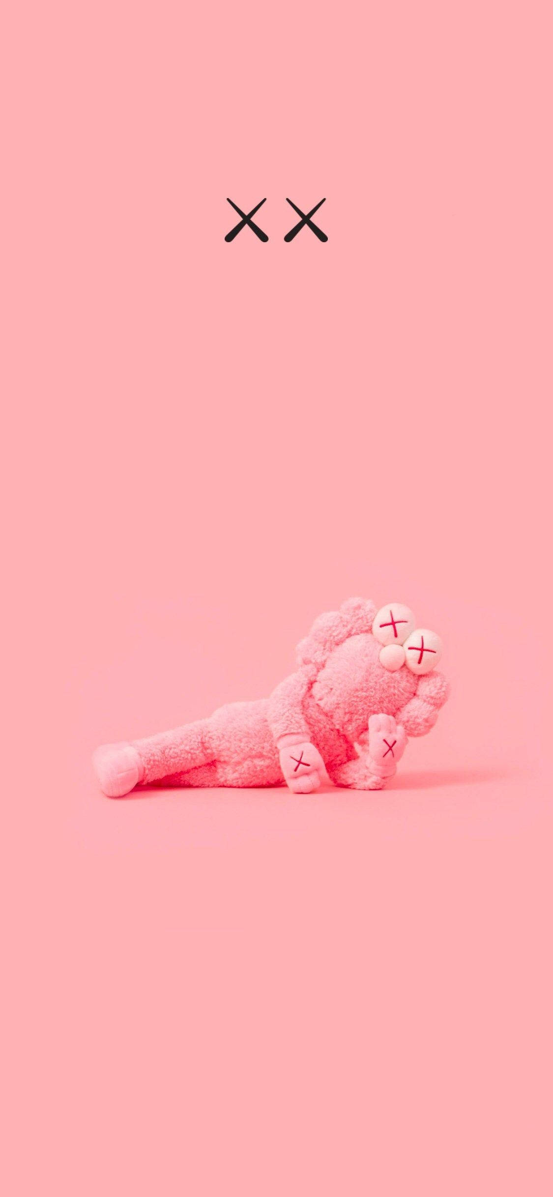 KAWS 桌布 壁紙 — 一個粉紅色毛絨KAWS玩偶放在純粉紅色背景上，上方有黑色XX標誌。