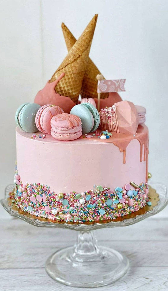 Birthday Cake 桌布 壁紙 — 一個粉紅色漸層蛋糕，裝飾著彩色糖粒、馬卡龍和兩個直立的冰淇淋甜筒，放在玻璃架上。