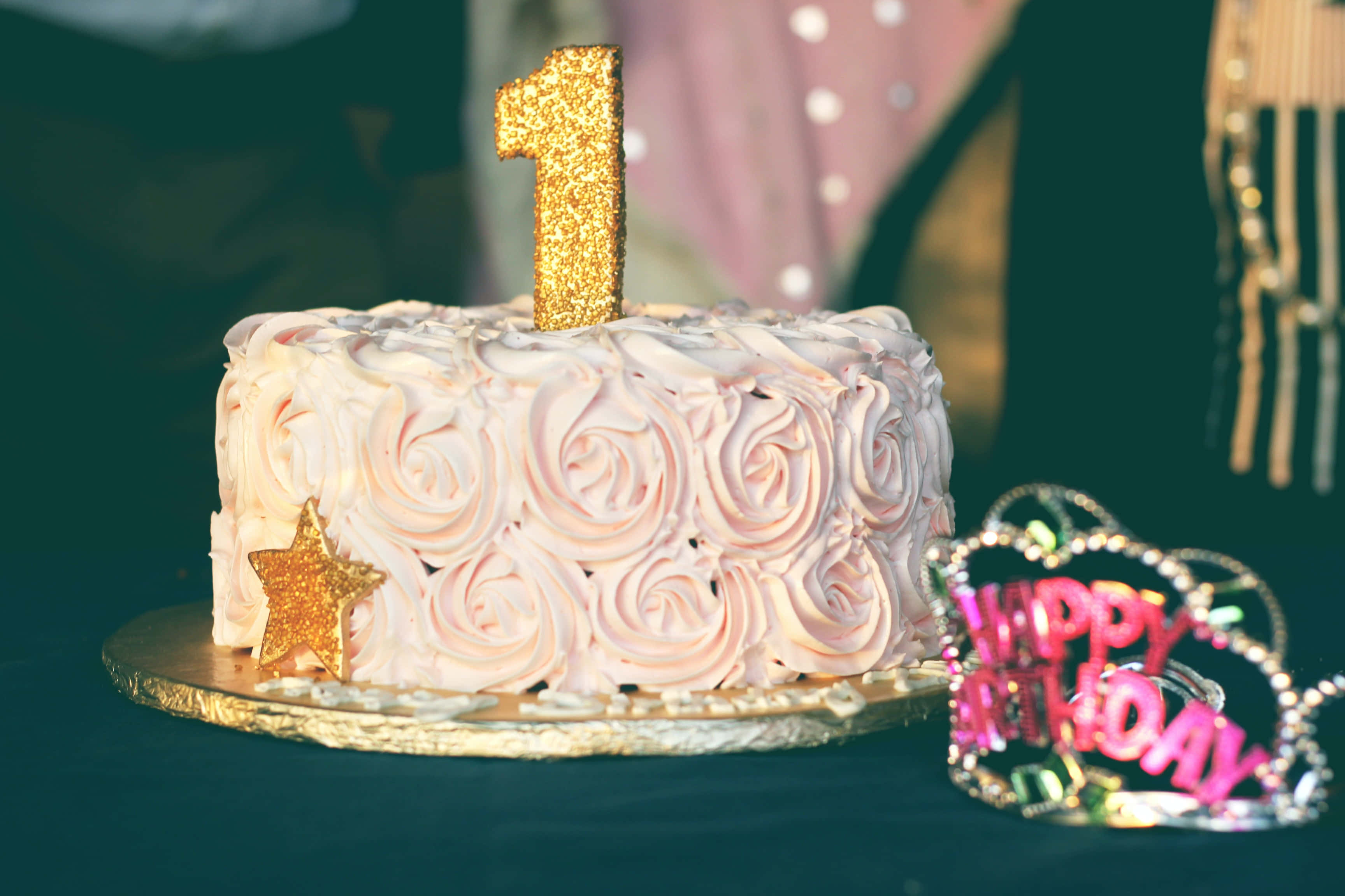 Cute Birthday 桌布 壁紙 — 一個粉紅色玫瑰花結糖霜生日蛋糕，上面有一個閃閃發光的金色數字一蠟燭，旁邊有一個閃亮的頭飾。