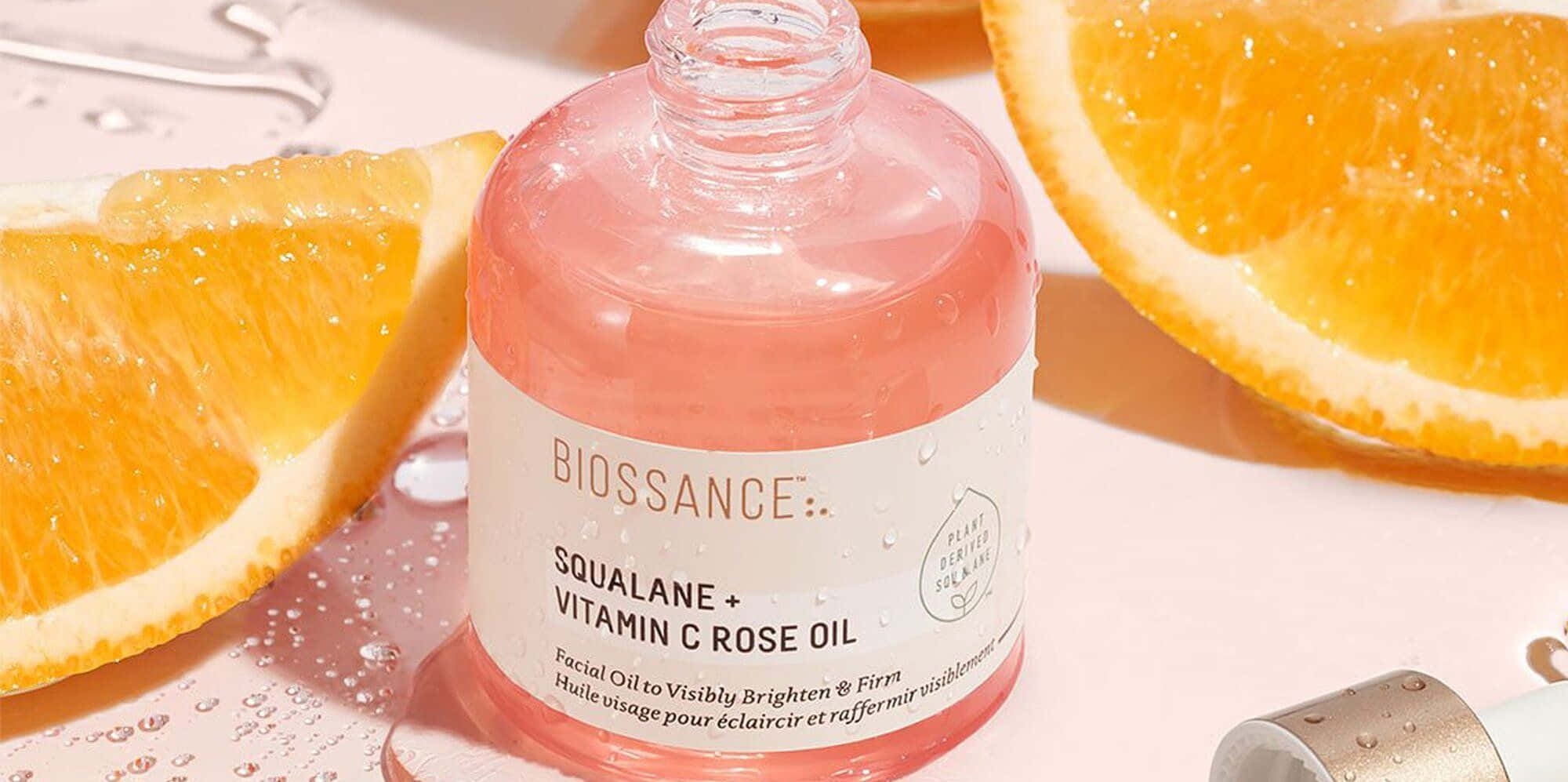 Rose Oil 桌布 壁紙 — 一個粉紅色的Biossance角鯊烷維生素C玫瑰油瓶，被新鮮橙片包圍在濕潤的表面上。