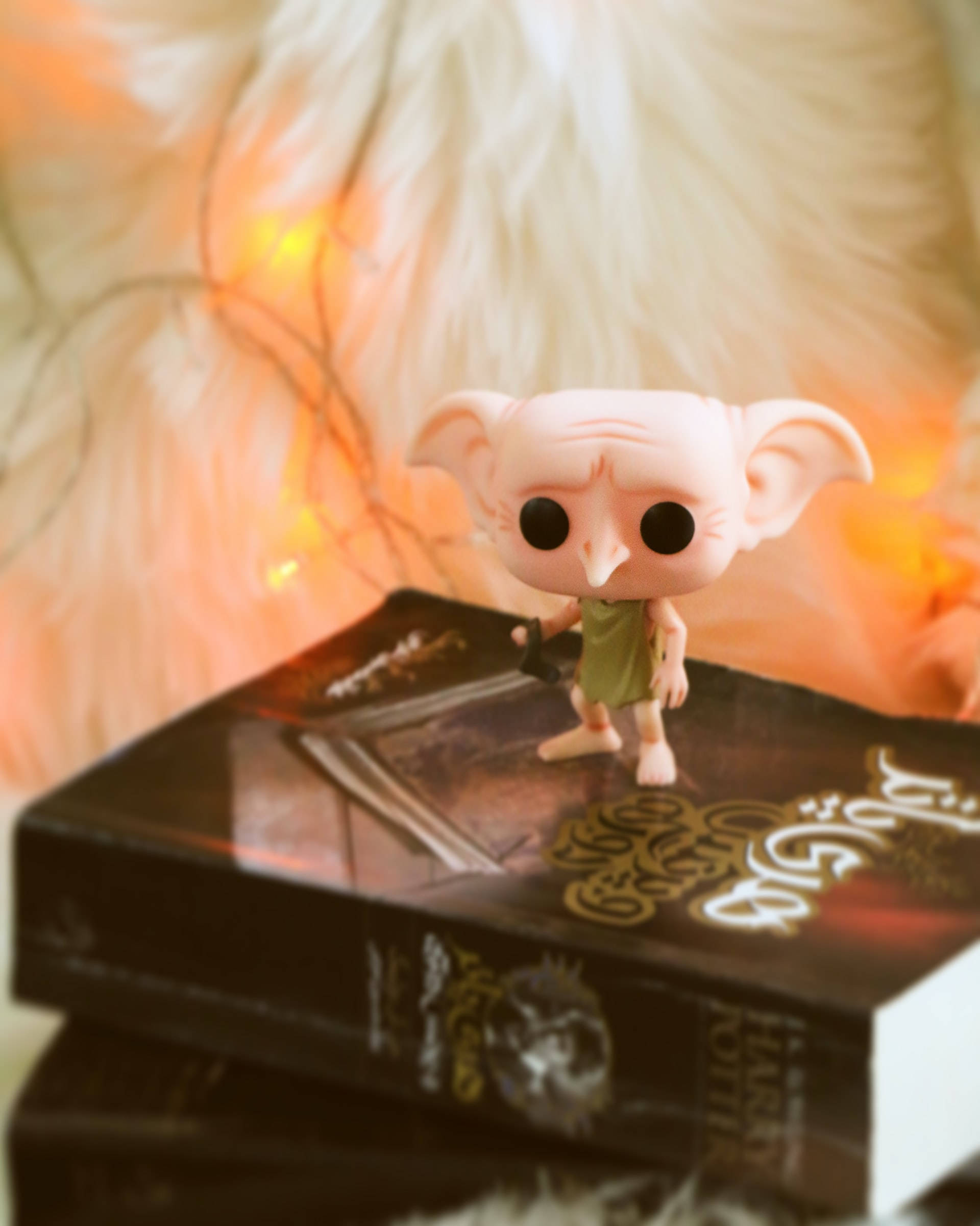 Elf 桌布 壁紙 — 一個粉紅色的多比 Funko Pop 人偶站在一堆哈利波特書籍上，背景是柔和發光的仙女燈。