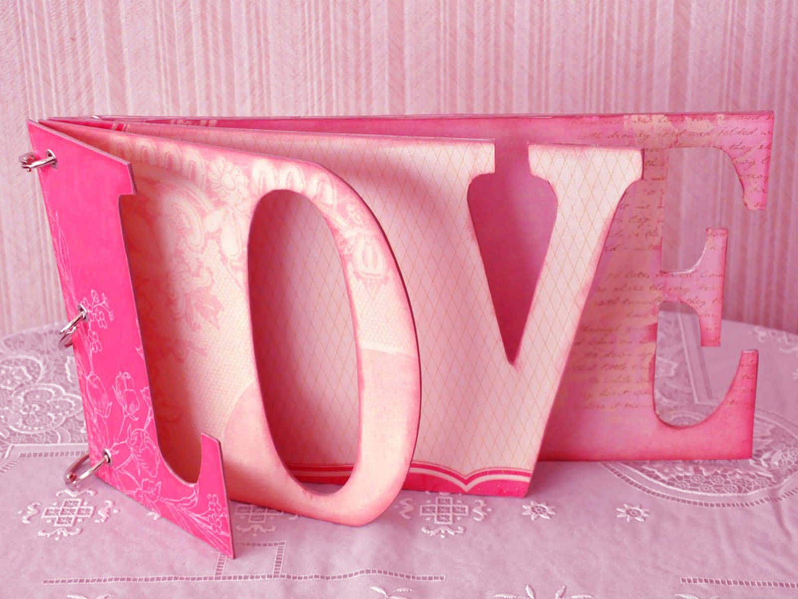 3d Love 桌布 壁紙 — 一個粉紅色紙剪字 LOVE 打開放在蕾絲桌布上，背景是條紋壁紙。