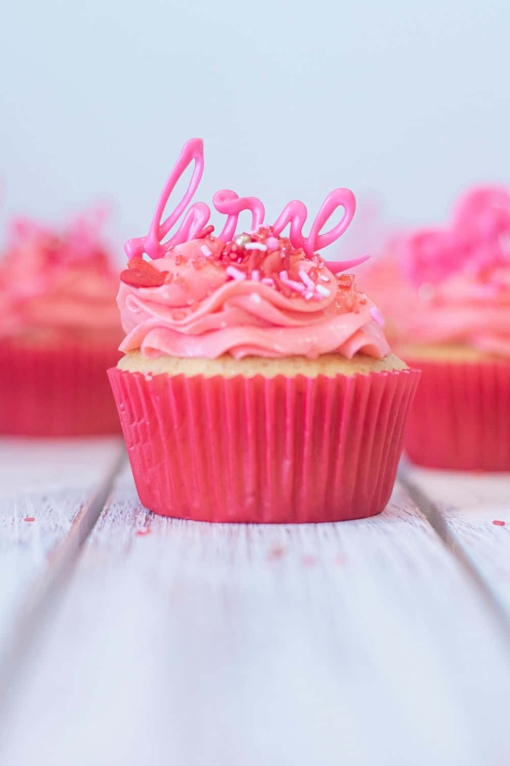 Pink Cupcakes 桌布 壁紙 — 一個粉紅色紙杯蛋糕的特寫，上面用粉紅色糖霜和彩針寫著「love」，放在白色木質表面上。