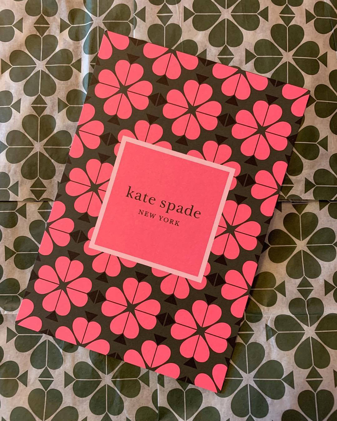 spade 桌布 壁紙 — 一個粉紅色花卉圖案的Kate Spade盒子放置在綠色幾何圖案表面上，以平鋪構圖呈現。