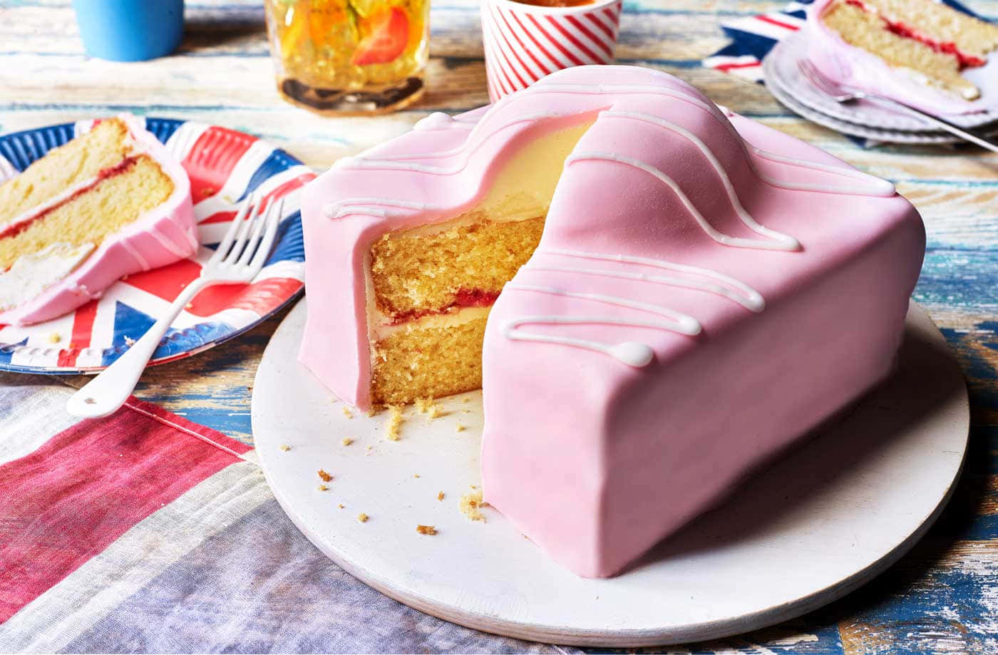 Cake Fondant 桌布 壁紙 — 一個粉紅色車形翻糖蛋糕，上面有白色糖霜，放在盤子上，旁邊有英國國旗盤子和一杯冰茶。