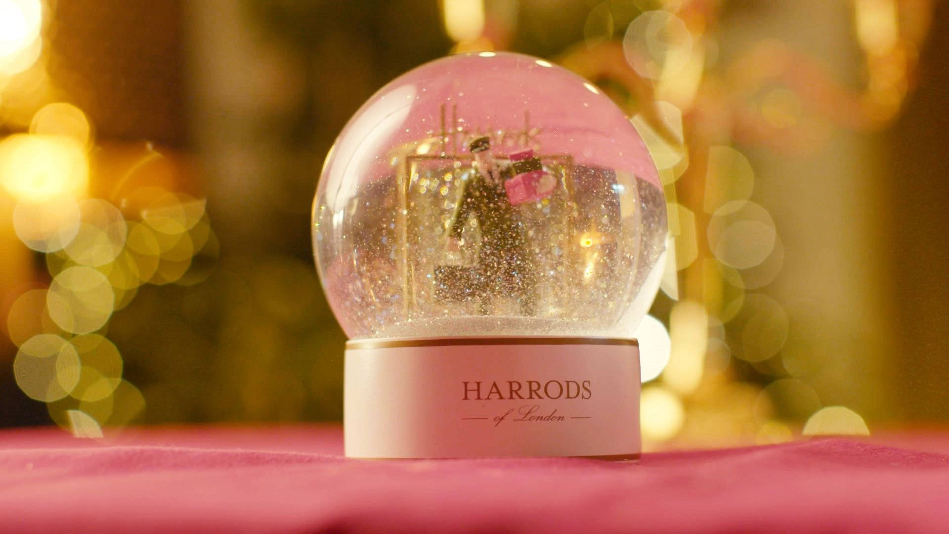 美學 桌布 壁紙 — 一個粉紅色雪花球，內有一對微型情侶，放置在粉紅色表面上，背景是溫暖的金色散景。