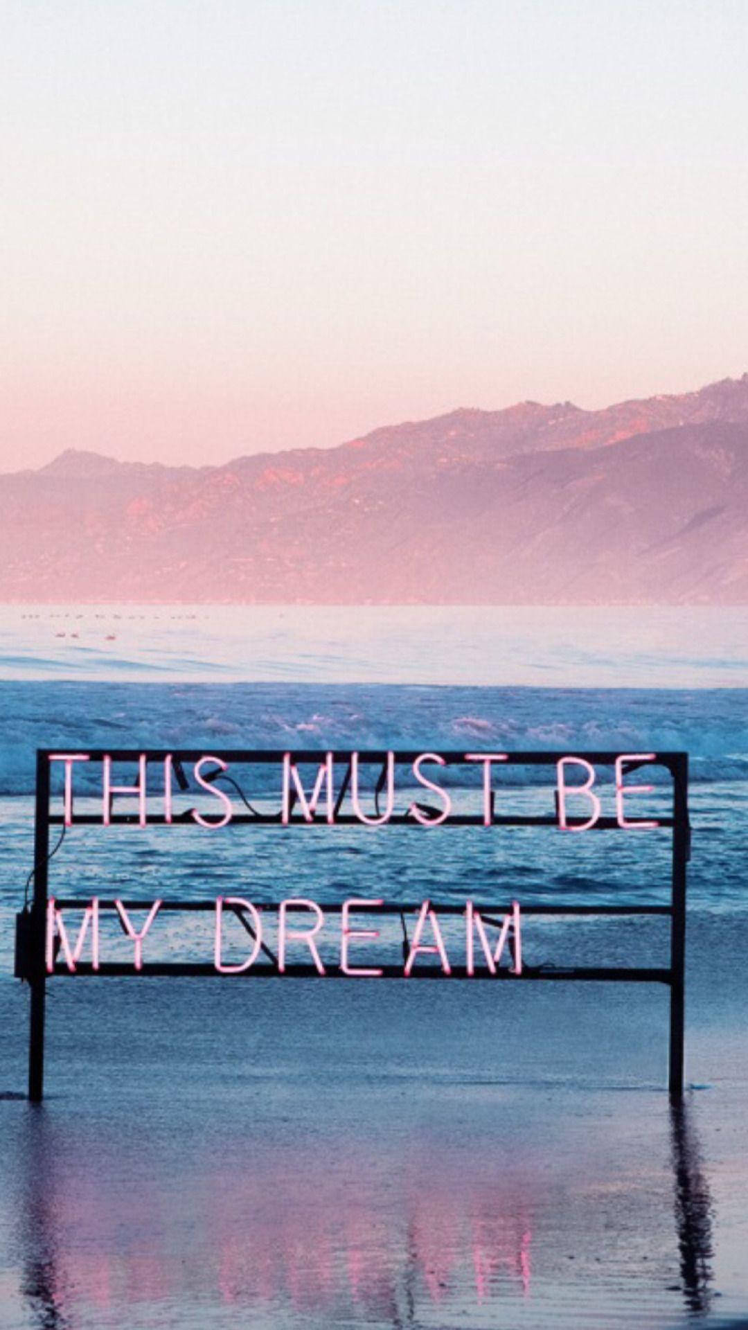 美學平板 桌布 壁紙 — 一個粉紅色霓虹燈牌寫著「THIS MUST BE MY DREAM」，矗立在黃昏時分的淺海水中，背景有山脈。