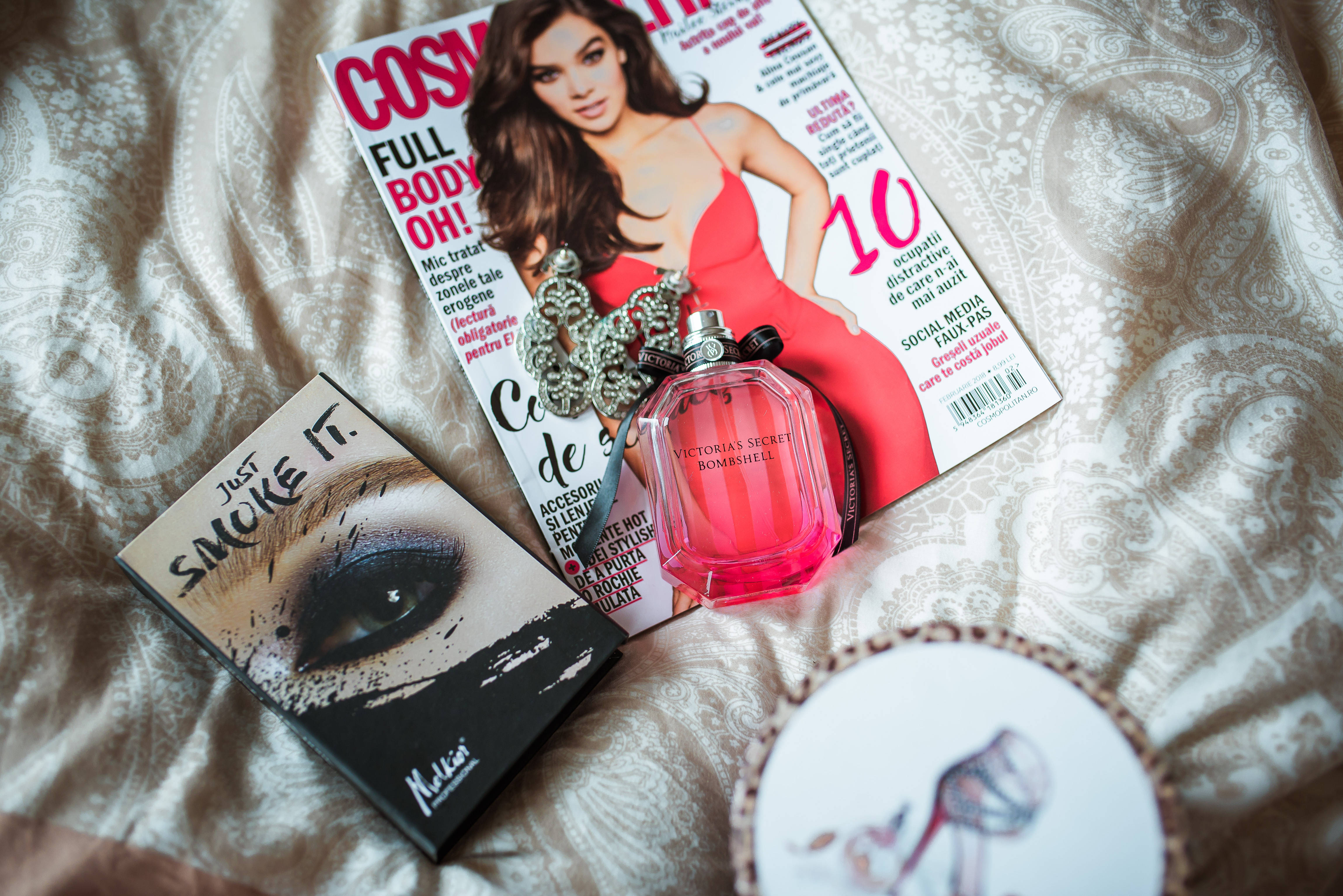 雜誌 桌布 壁紙 — 一個粉紅色香水瓶和Cosmopolitan雜誌放在有圖案的床罩上，旁邊有一個化妝盤和一個裝飾盤。