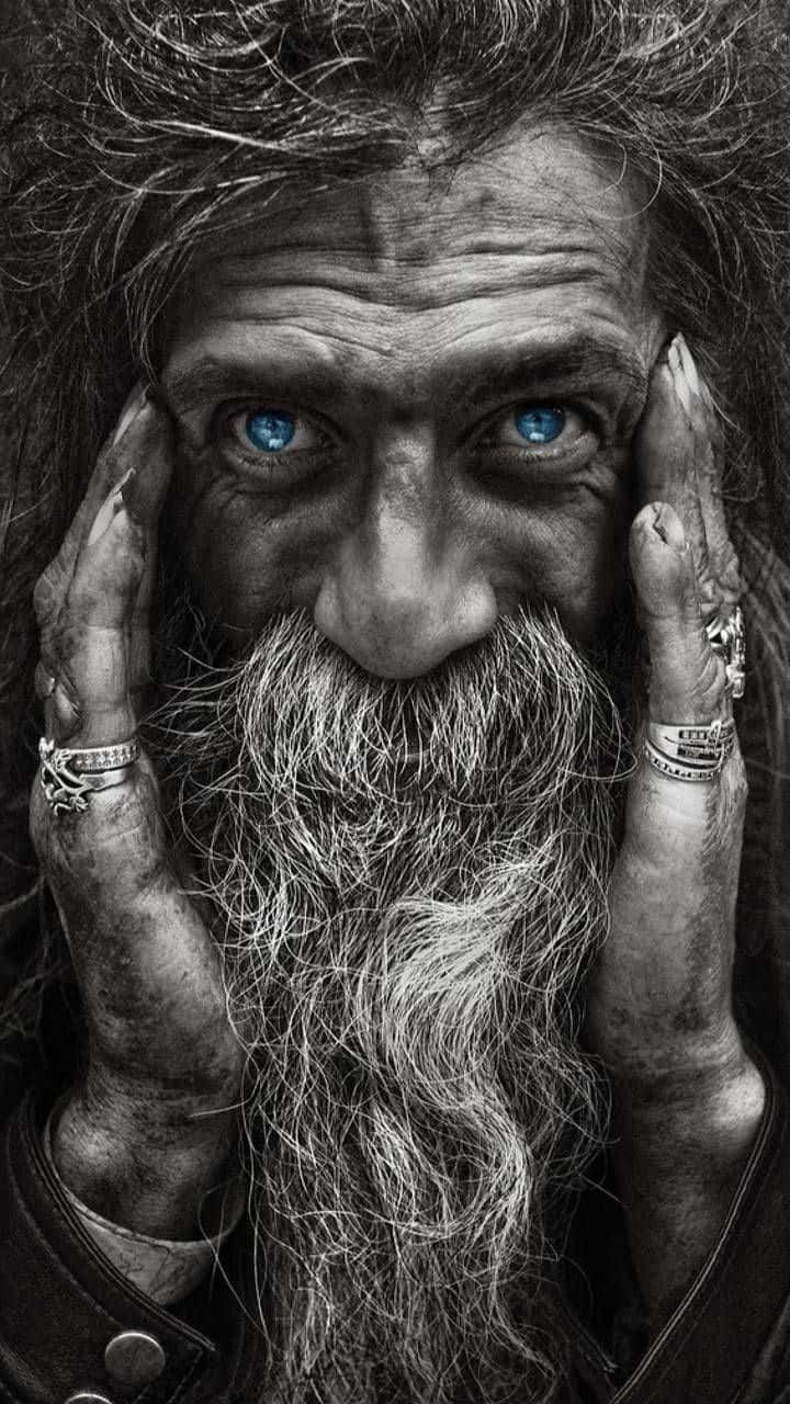 攝影 桌布 壁紙 — 一個粗獷男人的特寫肖像，他有銳利的藍眼睛和長鬍鬚，雙手戴著戒指框住臉龐。